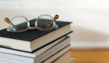 clear framed eyeglasses on top of pile of books